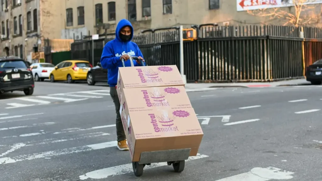Persona cargando cajas con una carretilla en la calle