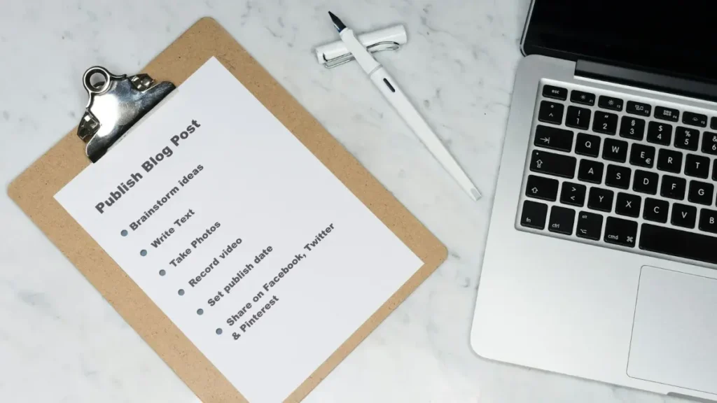 Lista de tareas en un portapapeles junto a un portátil